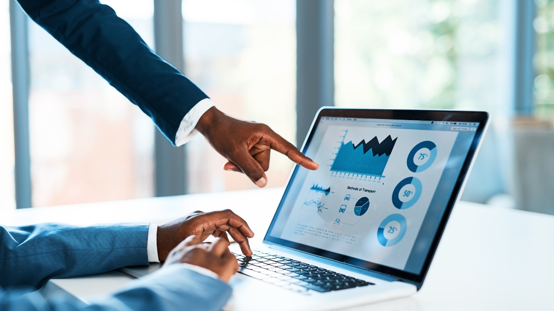 Two hands near a laptop looking at data graphs