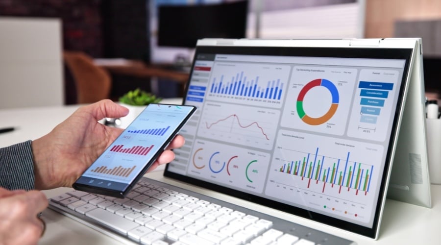 Person holding phone with data and looking at data on computer