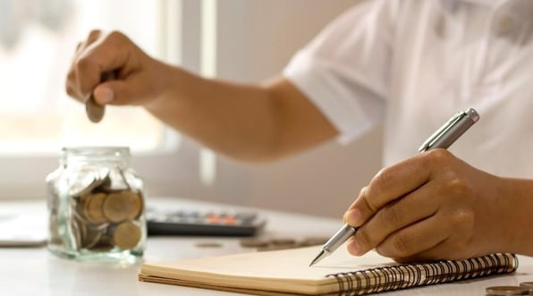 Someone budgeting and putting money in a glass jar